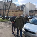 policja Zatrzymany mezczyzna prowadzony przez funkcjonariuszy przez policyjny parking do radiowozu